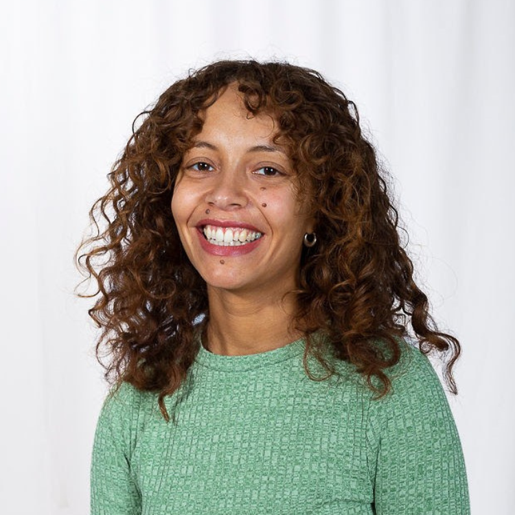 portrait sophia seawell Portrait of Sophia Seawell, smiling warmly at the camera. She has curly, shoulder-length hair and is wearing a green, short-sleeved top. The background is a simple white backdrop, highlighting her joyful expression.